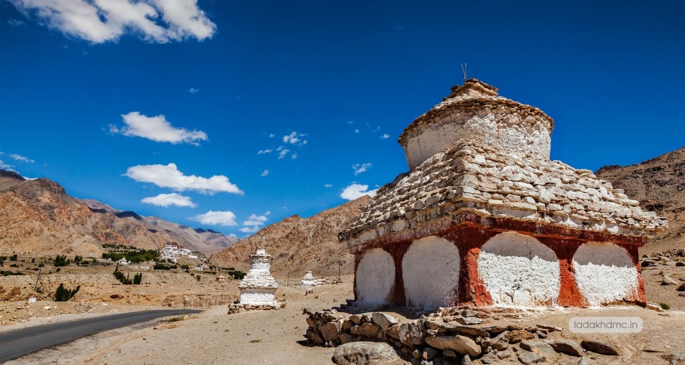 Interior of Chemrey Monastery prayer hall featuring monks and vibrant Buddhist murals in Ladakh